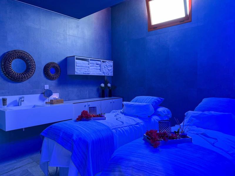 Room with two single beds under soft blue lighting, a small window, and a floating sink with mirrors.