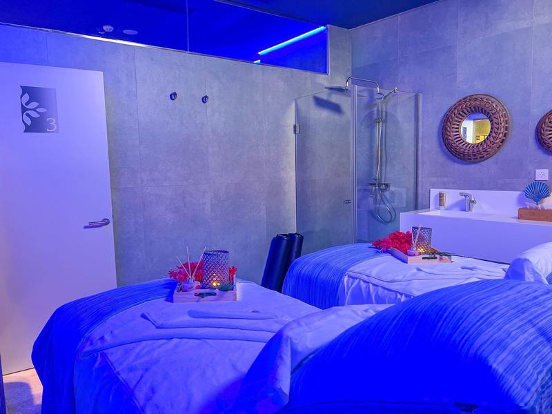 Modern hotel room with two single beds, blue lighting, and decorative mirrors on the wall.