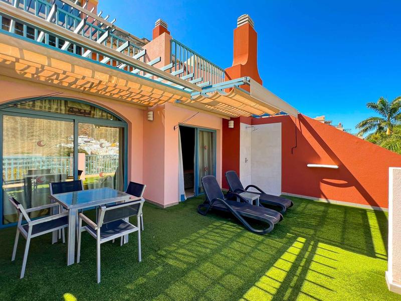 Sunny outdoor patio with glass table, chairs, and lounge chairs at a hotel.