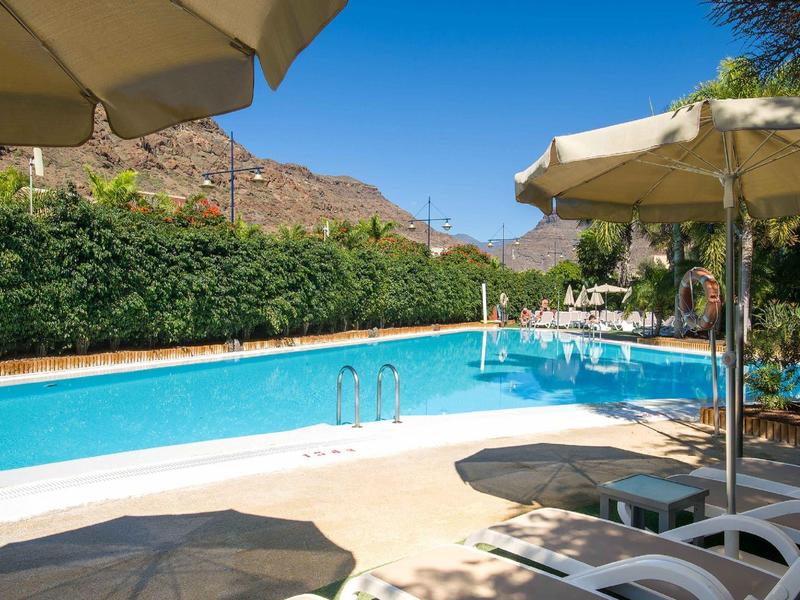 Outdoor pool with sun loungers and umbrellas in a sunny mountain setting.