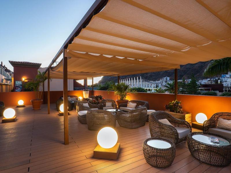 Hotel terrace with modern wicker furniture and glowing spherical lamps at dusk.