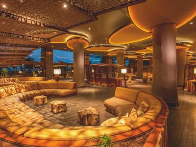 Gemütliche Lounge mit halbkreisförmigen Sofas, warmem Licht und Holzdecke in einem Raum.