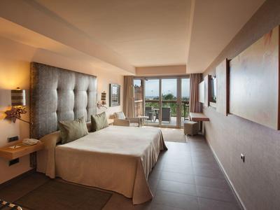 Modernes Hotelzimmer mit großem Bett, grauem Kopfteil, warmem Licht und Balkon mit Meerblick.