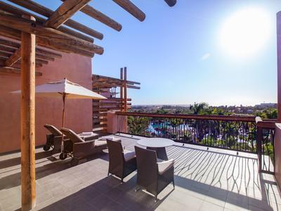 Große Terrasse mit Holzpergola, Sonnenliegen, Tisch und Blick auf Garten und blauen Himmel.