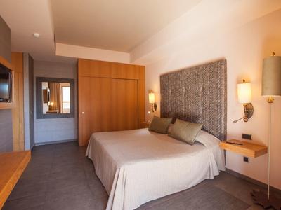 Modernes Hotelzimmer mit großem Bett, hellen Wänden, Holzschrank und weich gepolstertem Kopfteil.