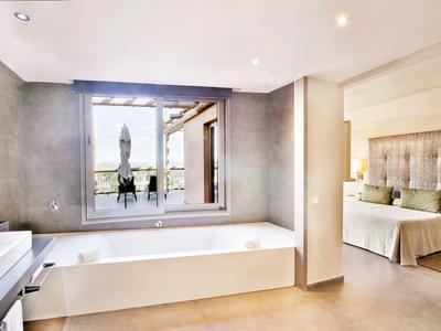 Moderner Raum mit weißer Badewanne, grauen Wänden und Sicht auf Schlafzimmer mit Bett.