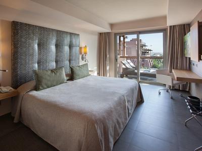Modernes Hotelzimmer mit großem Bett, grauen Wänden, Schreibtisch und Balkon mit Stadtblick.