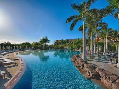 Velký venkovní bazén s palmami a lehátky pod jasnou oblohou v letovisku.