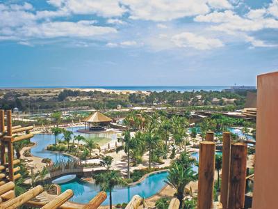 Blick auf tropischen Wasserpark mit Pools, Palmen und Sonnenschirmen unter blauem Himmel.