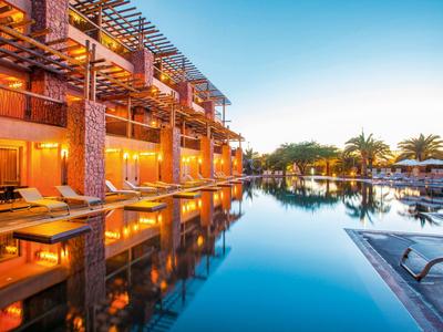 Moderner Hotelkomplex mit beleuchteten Balkonen und klarem Pool unter blauem Himmel.
