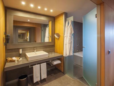 Modernes Badezimmer mit grauen Fliesen, weißem Waschbecken, großem Spiegel und Holzakzenten.