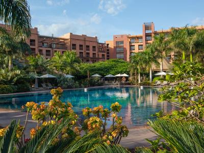Hotelový komplex s velkým bazénem obklopeným palmami a tropickou vegetací.