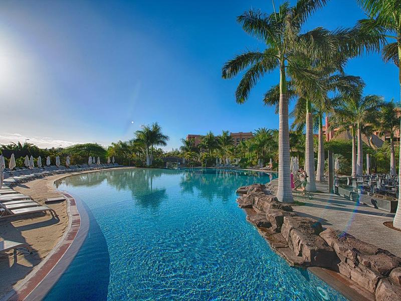 Basen na świeżym powietrzu otoczony palmami z leżakami do odpoczynku.