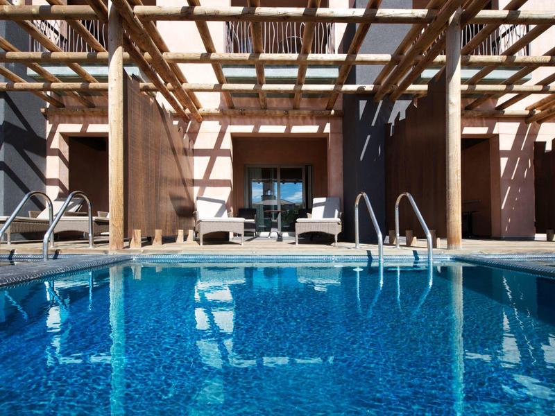 Czysty basen z leżakami i drewnianą konstrukcją pod słonecznym niebem.