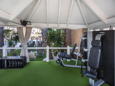 Moderner Fitnessbereich unter einem Pavillon mit Rasenboden und Geräten.