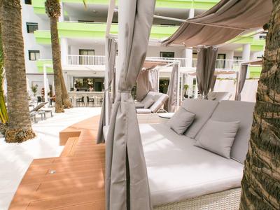 Buitenloungebed met kussens onder luifel bij palmbomen op hotelterras.