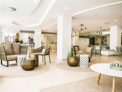 Helere hotelruimte met moderne zitplaatsen, ronde tafels en zachte neutrale tinten.