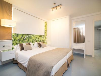Lichte hotelkamer met tweepersoonsbed, groene accentmuur en moderne witte meubels.