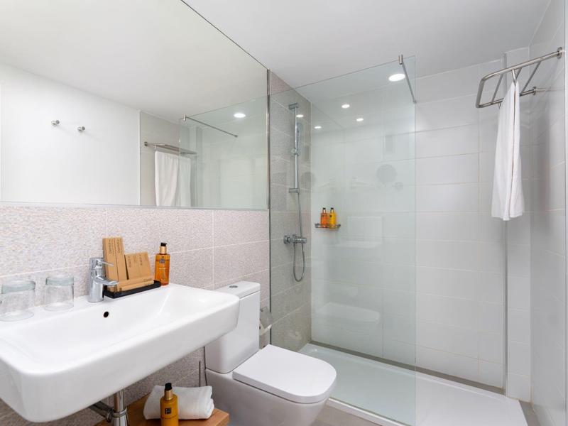 Moderne badkamer met witte wastafel, toilet en glazen douchecabine in een hotelkamer.