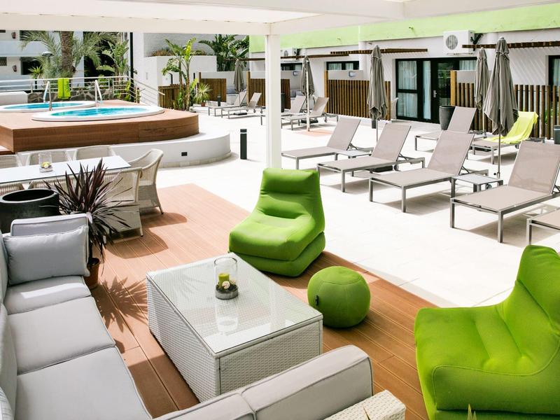 Moderne buitenlounge met groene stoelen, grijze banken, salontafel en zwembad op de achtergrond.