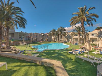 Ampia area piscina con lettini e palme in un complesso alberghiero sotto un cielo limpido.
