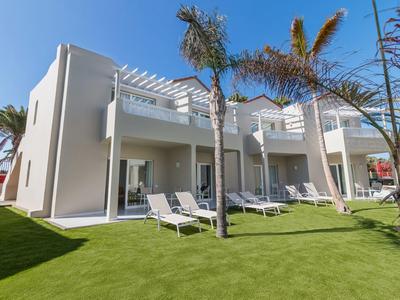 Edificio alberghiero moderno con lettini e palme su prato curato.