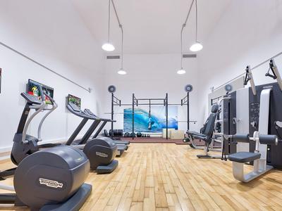 Gimnasio luminoso con equipos modernos, suelo de madera y gran pantalla en la pared.