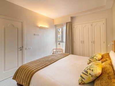 Camera d'hotel luminosa con letto grande, copriletto marrone, cuscini e armadio in legno.