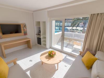 Camera d'hotel luminosa con divano, tavolino e terrazza con vista sul mare.