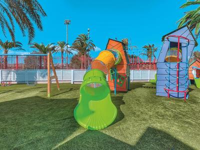 Area giochi colorata per bambini con scivolo e strutture da arrampicata su prato sotto il sole.