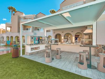 Área de bar exterior moderna con asientos y césped frente a un hotel.