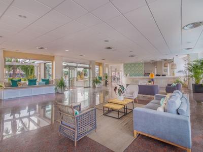 Área luminosa del vestíbulo del hotel con sofás modernos, plantas y recepción al fondo.