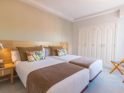 Camera d'hotel luminosa con due letti singoli, comodini e grande armadio.