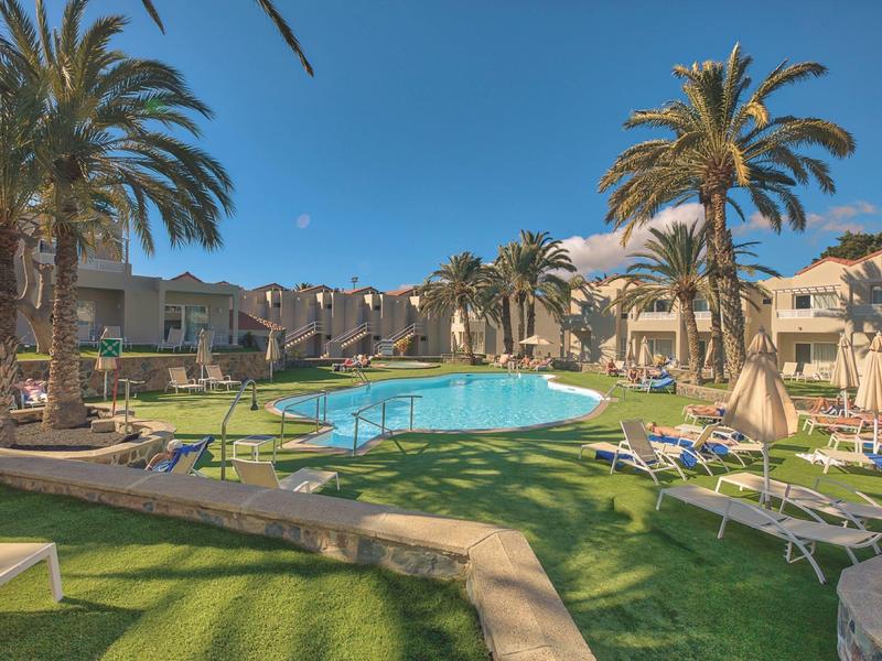 Ampia area piscina con lettini e palme in un complesso alberghiero sotto un cielo limpido.
