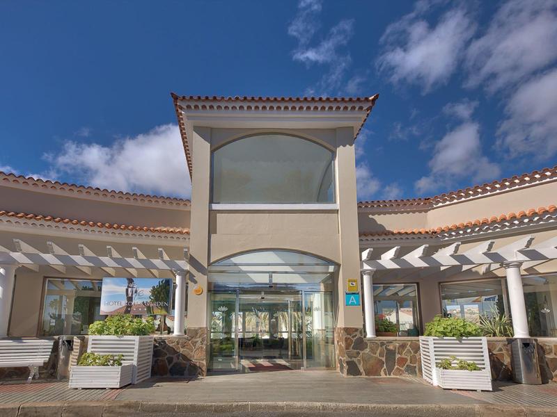 Ingresso dell'hotel con facciata in vetro, pergola e cielo ampio di giorno.