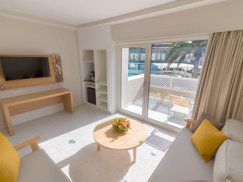 Camera d'hotel luminosa con divano, tavolino e terrazza con vista sul mare.