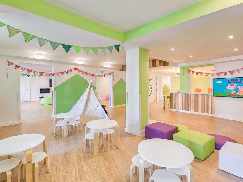 Area giochi luminosa e adatta ai bambini con cuscini colorati, tavoli e una piccola tenda.