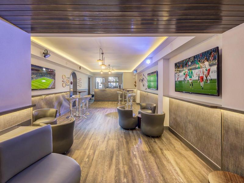 Area lounge moderna dell'hotel con pavimenti in legno, sedute grigie e grande TV a schermo piatto.