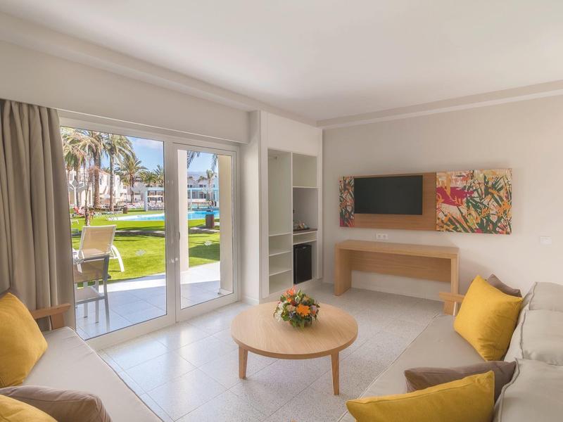 Soggiorno luminoso con divani, cuscini gialli e vista su giardino curato attraverso grandi finestre.