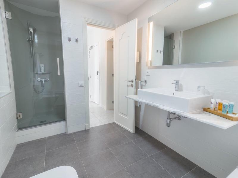 Bagno luminoso con ampia doccia, doppi lavandini e pareti bianche.