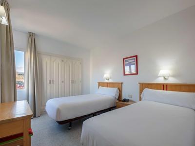 Chambre d'hôtel lumineuse avec deux lits simples, bureau et armoire.