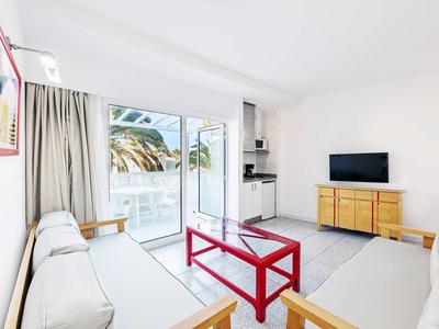 Salon lumineux avec mobilier blanc, table basse rouge et accès balcon avec vue sur la mer.