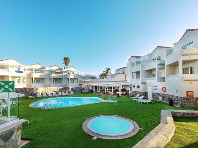 Complexe hôtelier avec deux piscines, bâtiments blancs et pelouse verte sous un ciel bleu.