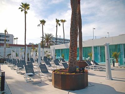 Moderne Terrasse mit Liegestühlen, Schirmen und Palmen bei bewölktem Himmel.