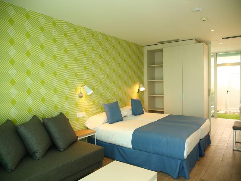 Modernes Hotelzimmer mit Doppelbett, grün gemusterter Wand, Sofa und großem Fenster.