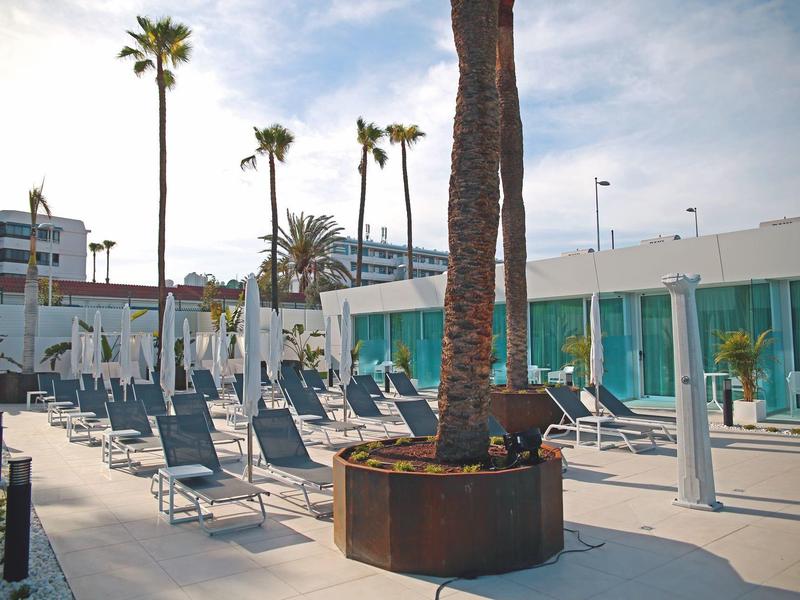 Moderne Terrasse mit Liegestühlen, Schirmen und Palmen bei bewölktem Himmel.