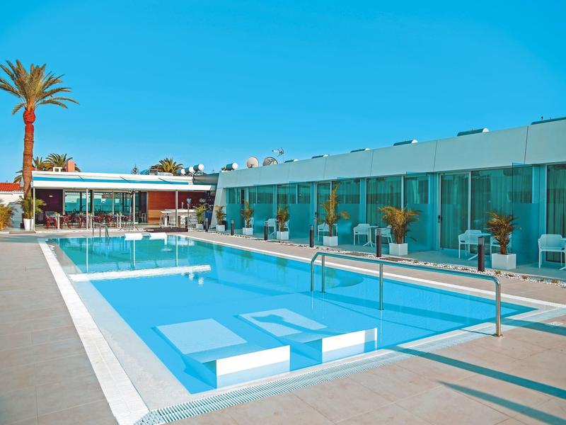 Moderner Außenpool mit klarem Wasser, Sonnenterrasse, Palmen und Glasfront eines Gebäudes.