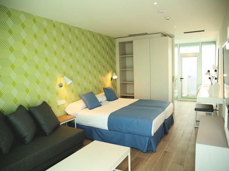 Modernes Gästezimmer mit großem Bett, grün gemusterter Wand, Sofa und hellem Holzboden.