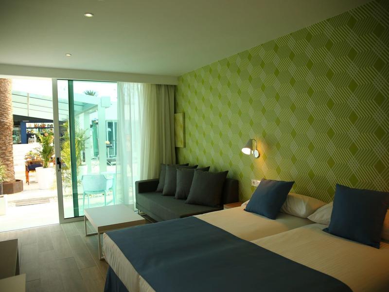 Modernes Hotelzimmer mit Doppelbett, grüner Tapete, grauen Kissen und Terrasse mit Glas-Schiebetür.