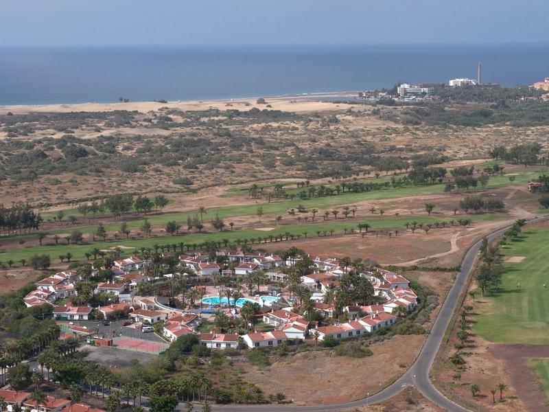 Veduta aerea di un villaggio turistico con edifici bianchi, circondato da terra asciutta e vista sul mare